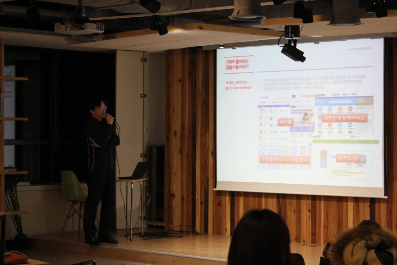 the man stands in front of a projector with a projector screen behind him