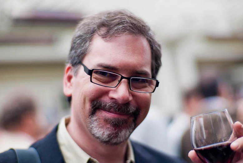 the man smiles while holding a glass of red wine