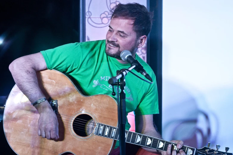 a man holding an acoustic guitar near a microphone