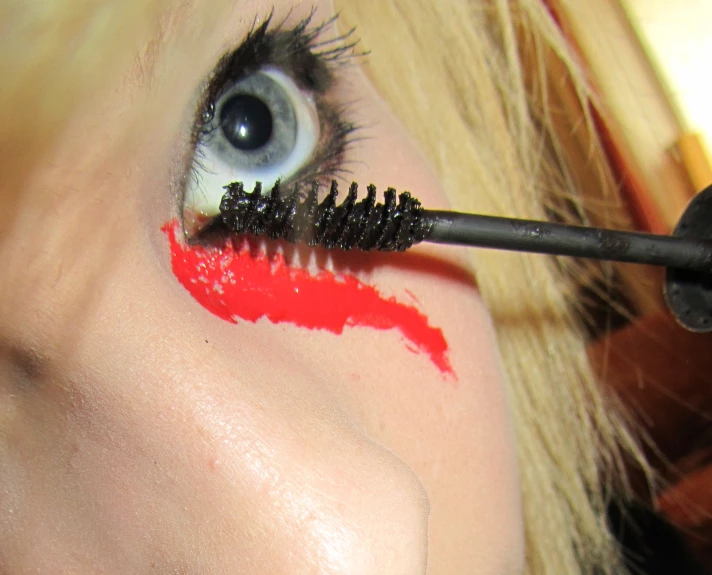 a woman is holding a mascara and eyeliner brush