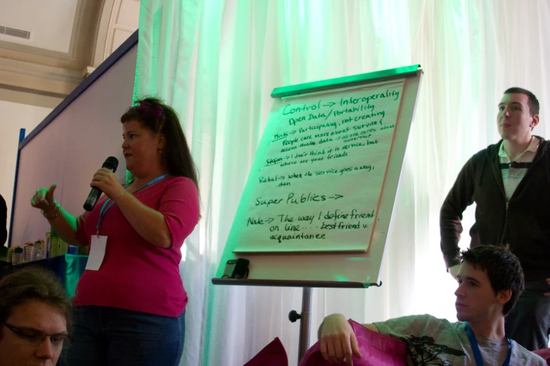 a man giving a speech while someone behind is writing on a white board