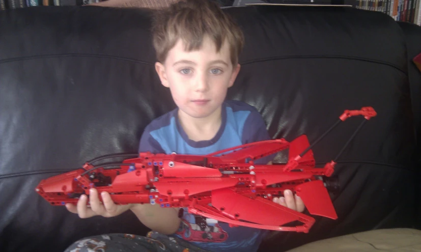 a boy sitting on a couch with a red model of a fighter jet