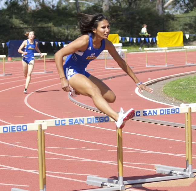 a woman is running over a hurdle on a track