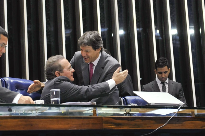 four men sitting at a table in suits shaking hands