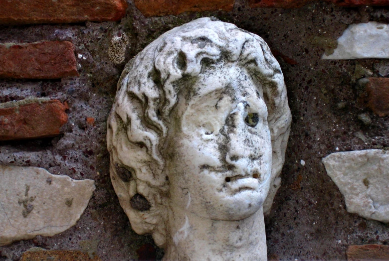 a statue of a female head with brick walls behind it