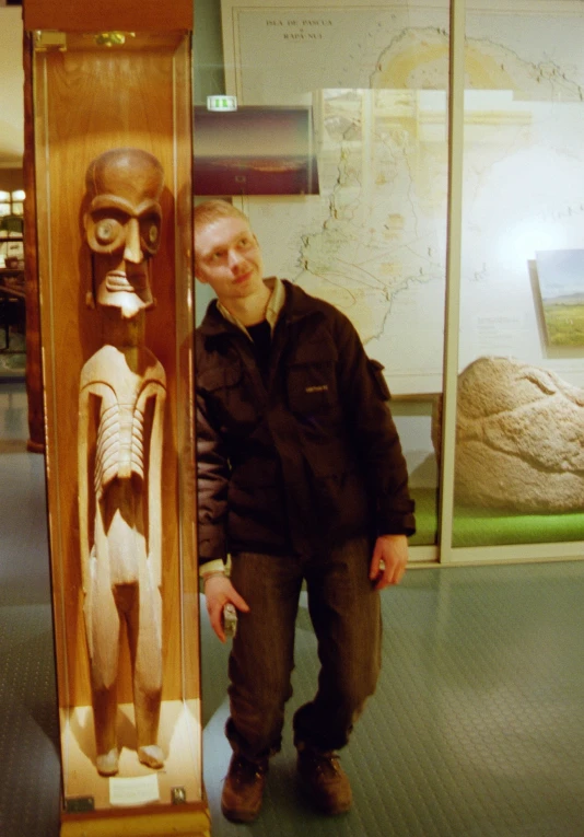 a man standing beside a carved wooden skeleton in a museum