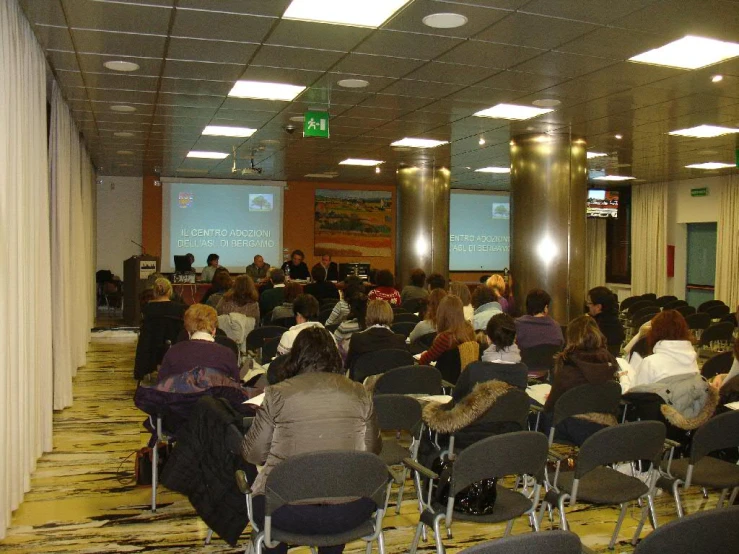 a classroom with chairs full of people at long rows and onlookers