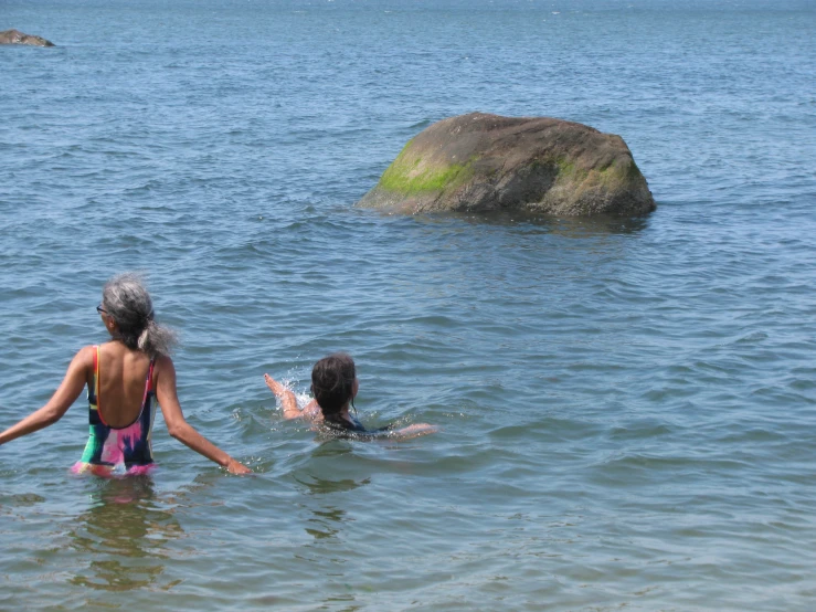 two children swimming in the ocean near rocks