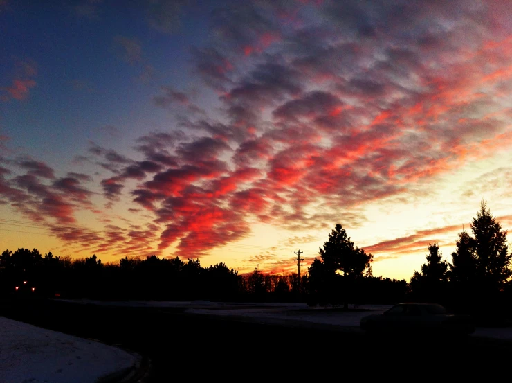 sunset with clouds above the trees and snow covered road