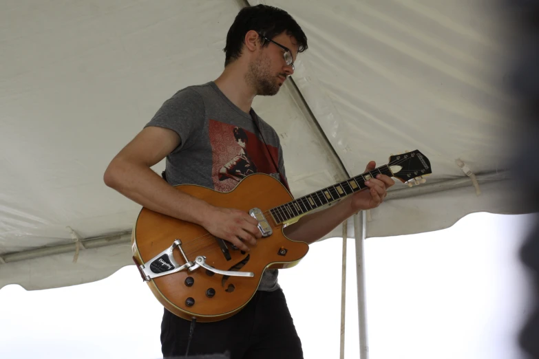 a man in glasses playing guitar under a white tent