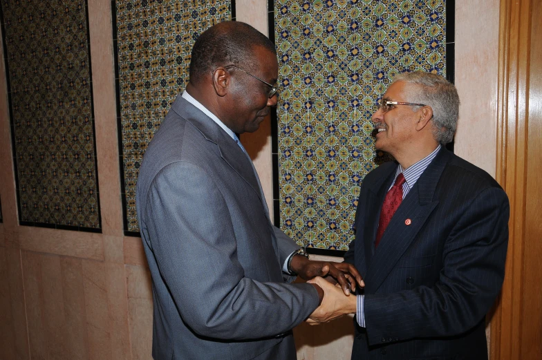 two men in business attire meet while one holds the other's hand