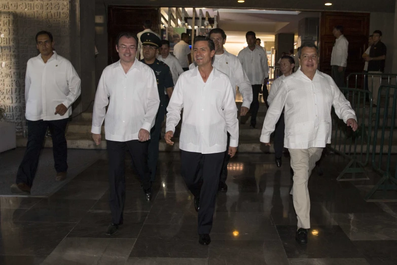 several men in white shirts are walking down the hall