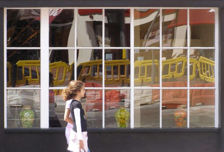 a girl walking by a large store window reflecting a yellow bus