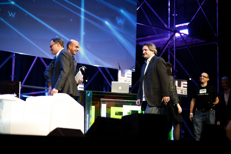 three men are standing in front of a big screen