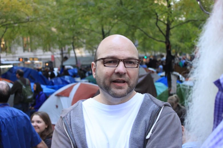 a man wearing glasses standing with other people in the background