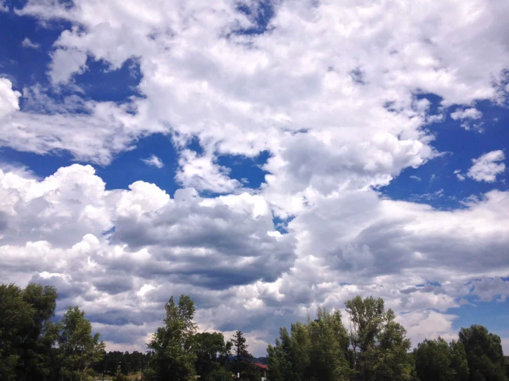 some white clouds and blue sky with green trees