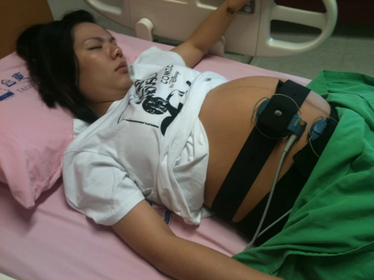 a pregnant woman laying in a hospital bed with her arm stretched up