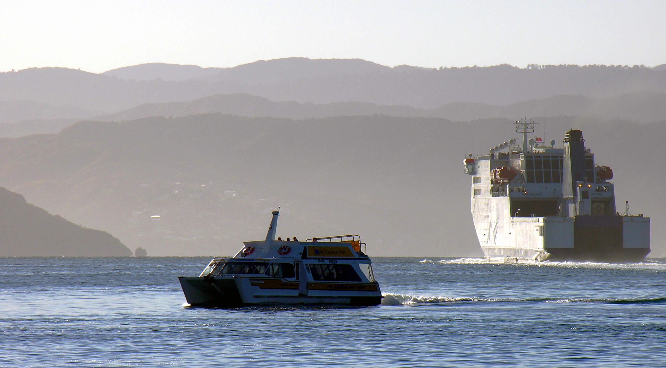 a ship sailing past a boat in a bay with hills behind it