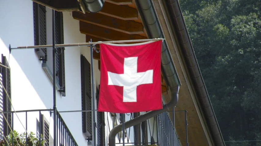the swiss flag hanging from the building is flown by the balcony
