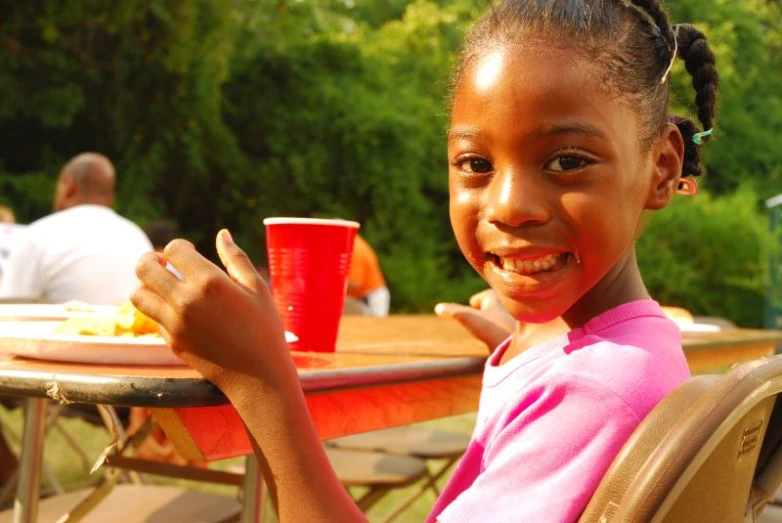 a small child smiles while sitting at a picnic table