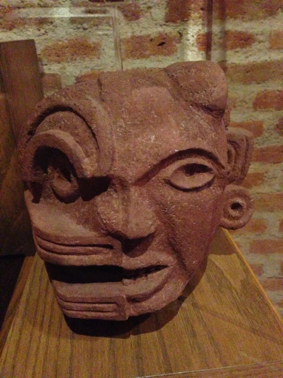 a wooden sculpture of a face is next to a brick wall