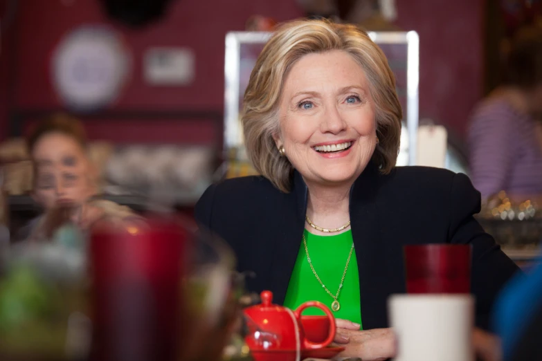 a woman sits at a table with mugs and smiles