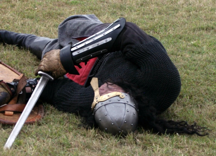 a knight laying on the ground in armor with his head on a sword