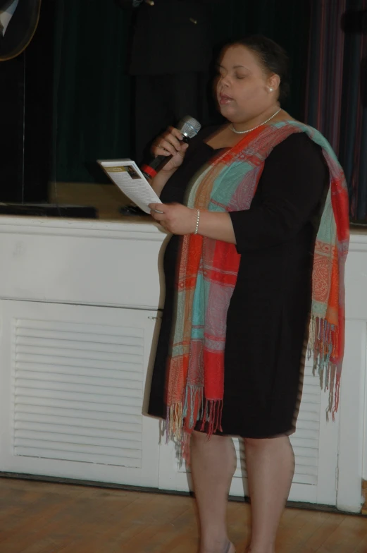 a woman in a black dress and colorful scarf holding a microphone