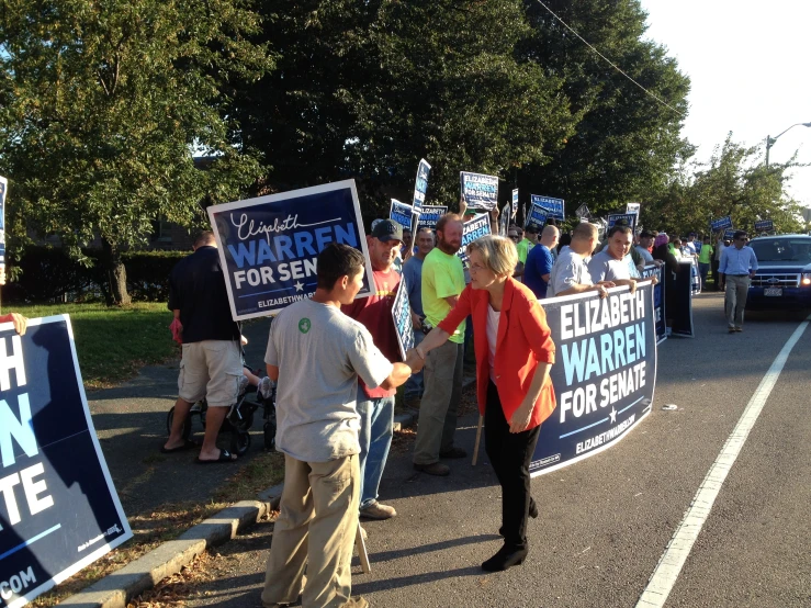 people stand on the side of a street and hold up signs