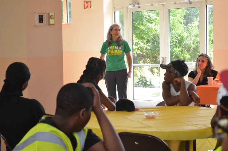 a woman in a green shirt speaks to a group of people