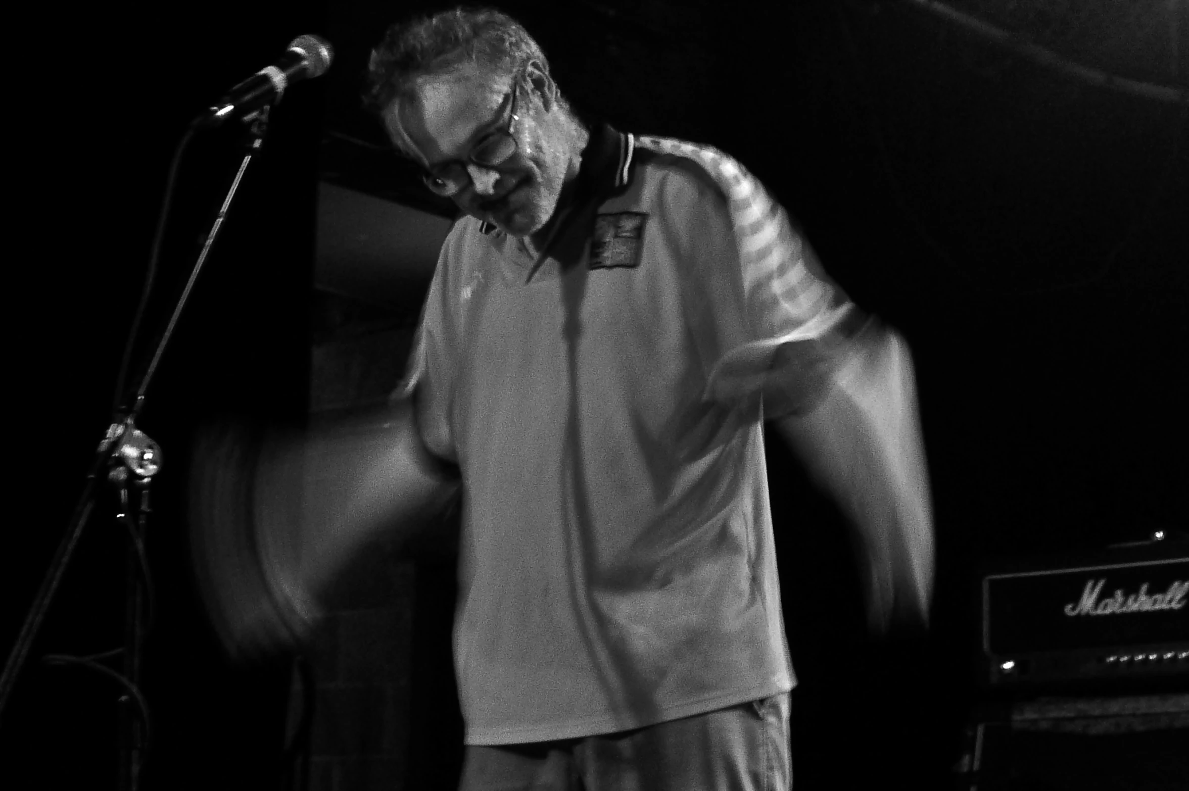 a man in glasses and a shirt is at a microphone and a guitar case