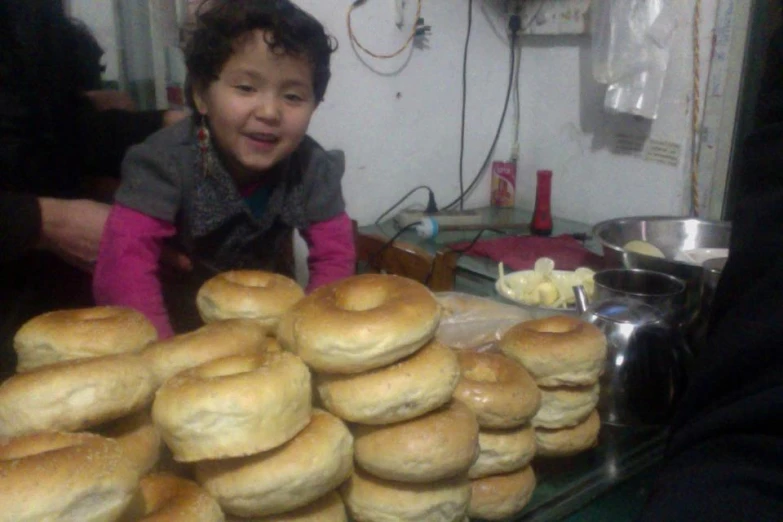 a little girl sitting in front of many bread rolls
