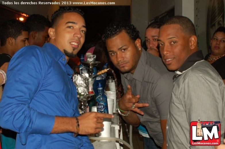 three men standing around at a bar with drinks on a table