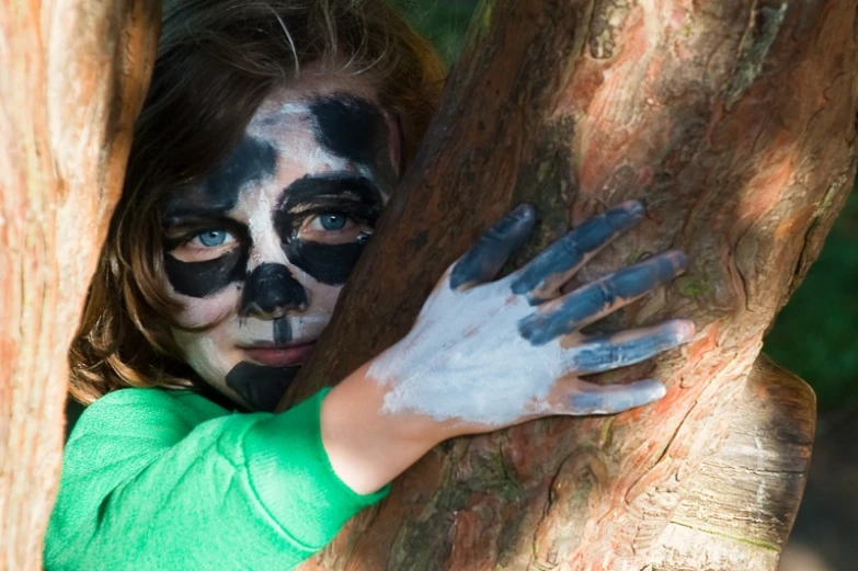 child with face painted to look like a bear hugging tree