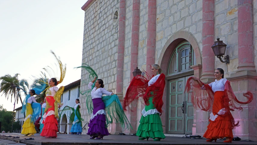 some colorful women with long tails and umbrellas dance on the street