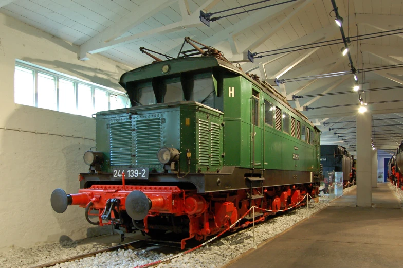 a red and green locomotive sits next to other trains