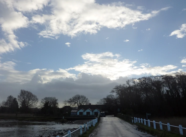 a road with clouds in the sky and houses on the other side