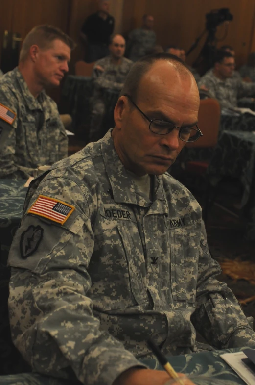 a man in uniform sits in a room full of others