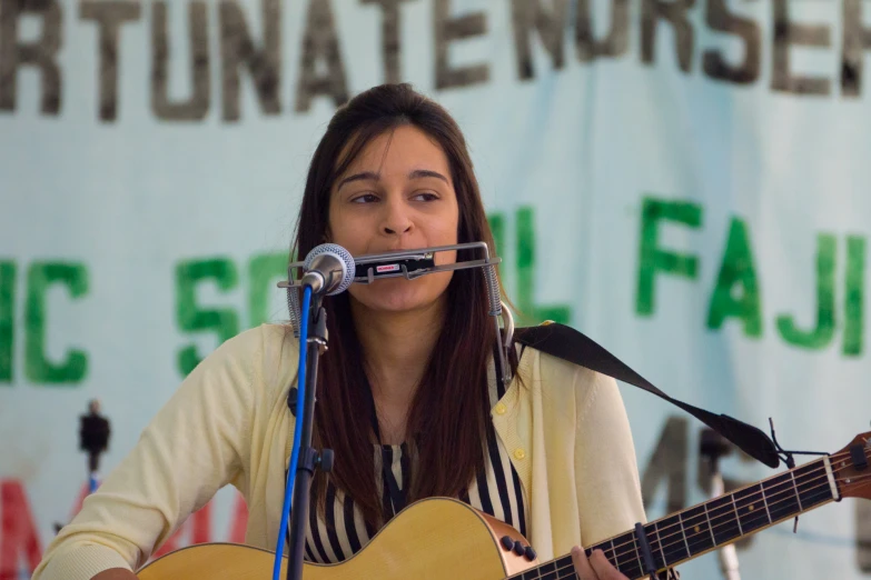 a woman singing into a microphone and holding an acoustic guitar