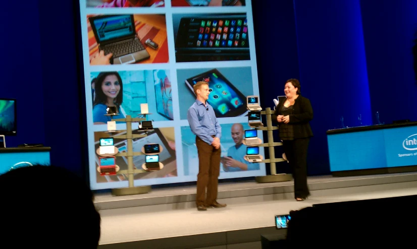 two people stand at a stage with some electronic devices on it