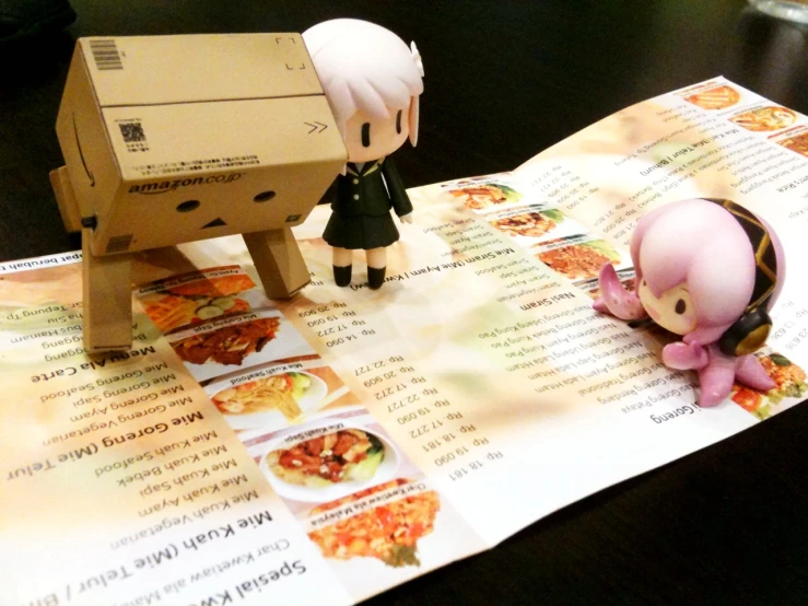 a small plastic figurine stands beside a pizza box sitting on top of an open menu