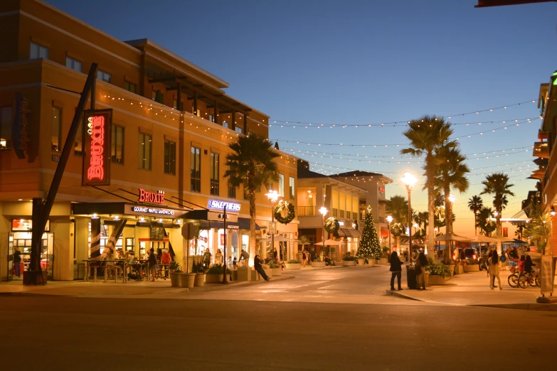 a street with people standing on the sidewalk and palm trees