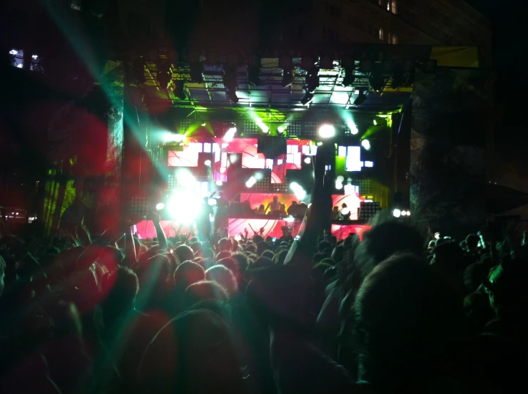 a crowd is shown at night in front of a stage with multiple colored lights