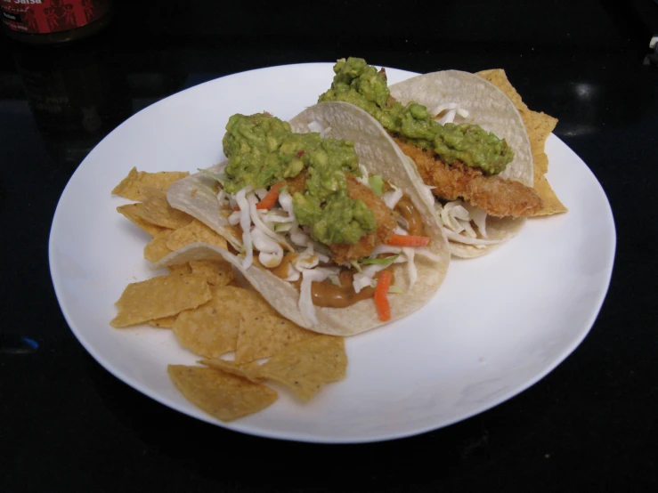 two tacos with guacamole and tortillas on white plate