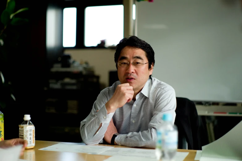 a man sitting at a desk holding his hand up to his chin