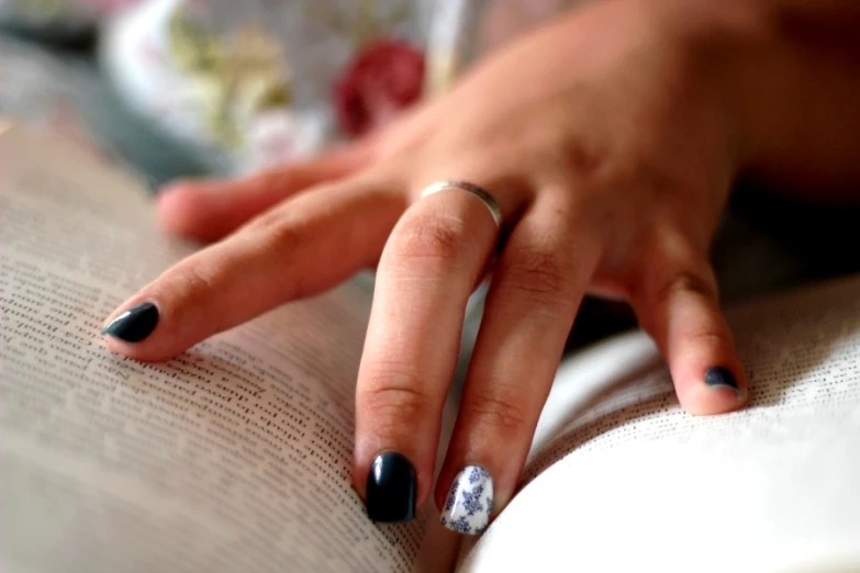 a woman with black fingernails holds up an open book