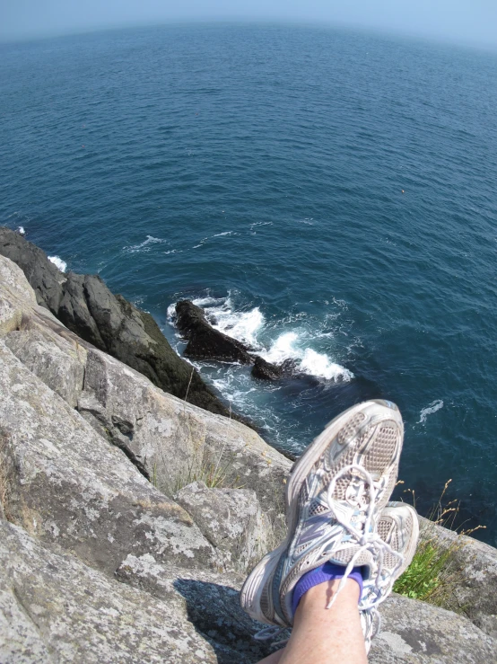 someones feet and a pair of shoes are overlooking the ocean