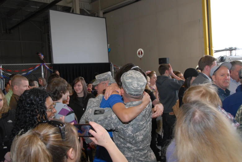 military men hug each other in the middle of a room full of people