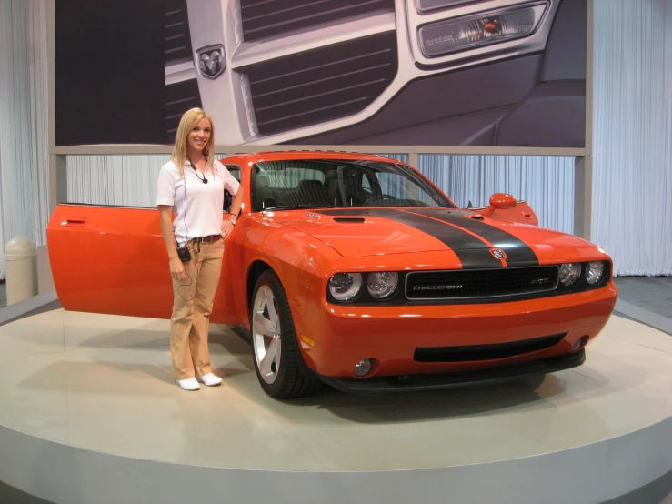 a woman standing next to a large orange car