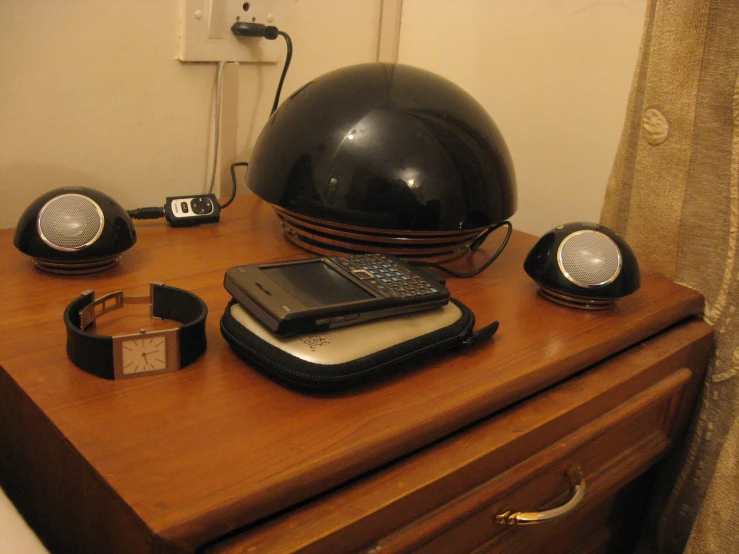 a wooden nightstand topped with a lamp, cellphone, and camera